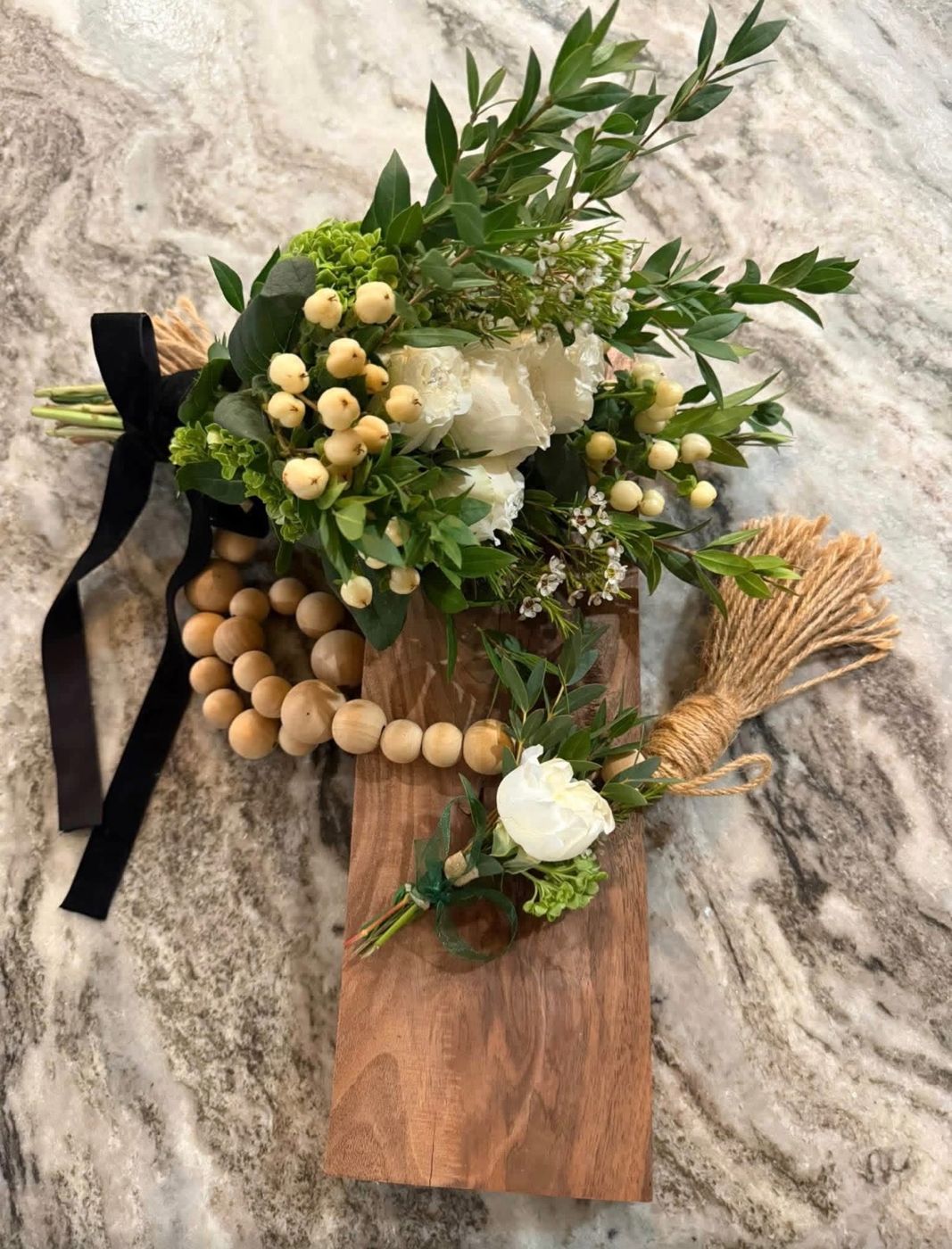 White prom bouquet tied with black velvet ribbon and matching boutonnière on a wood board