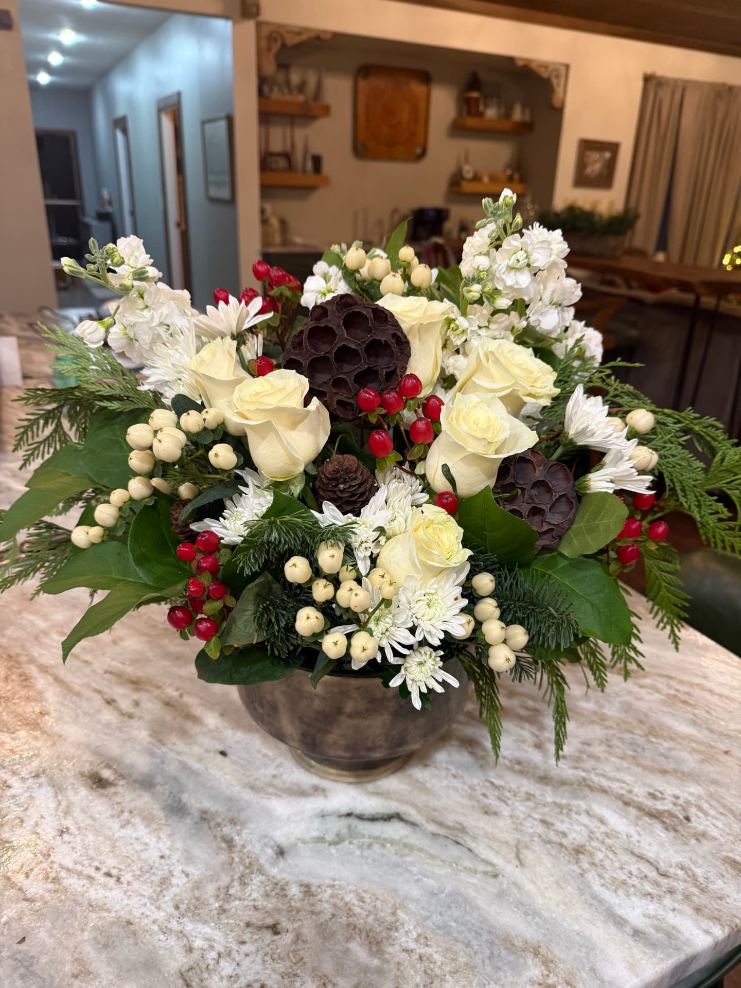 Winter arrangement of white roses, red and cream berries, lotus pods and evergreen in a bronze bowl