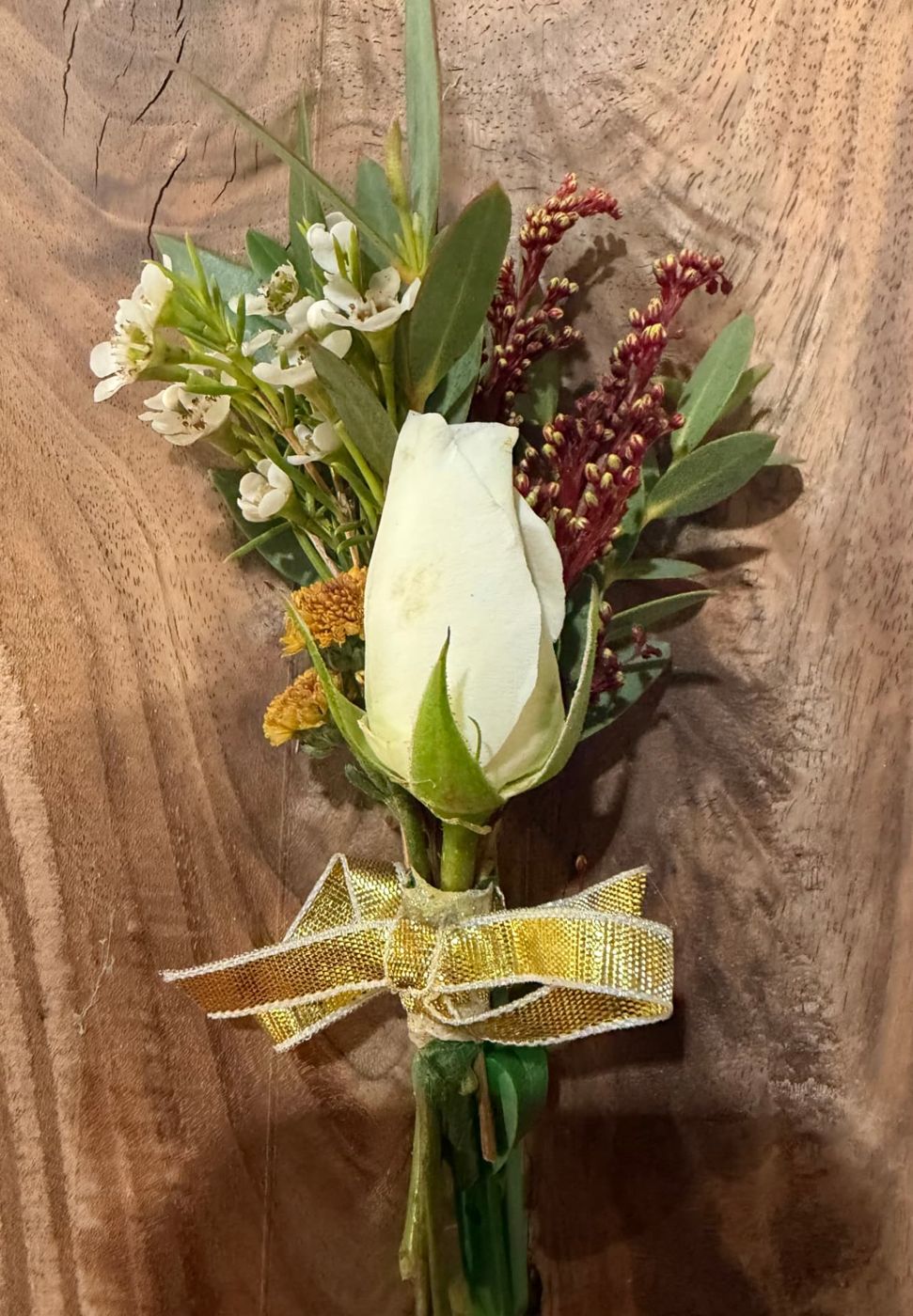 White rose boutonnière with wax flower and a gold ribbon on wood