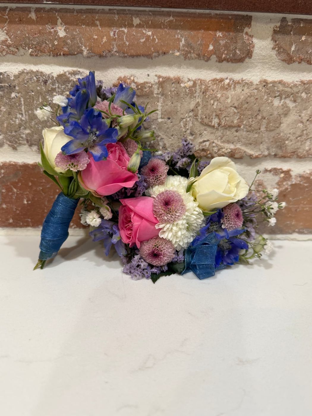 Pink roses and blue delphinium corsage set against brick