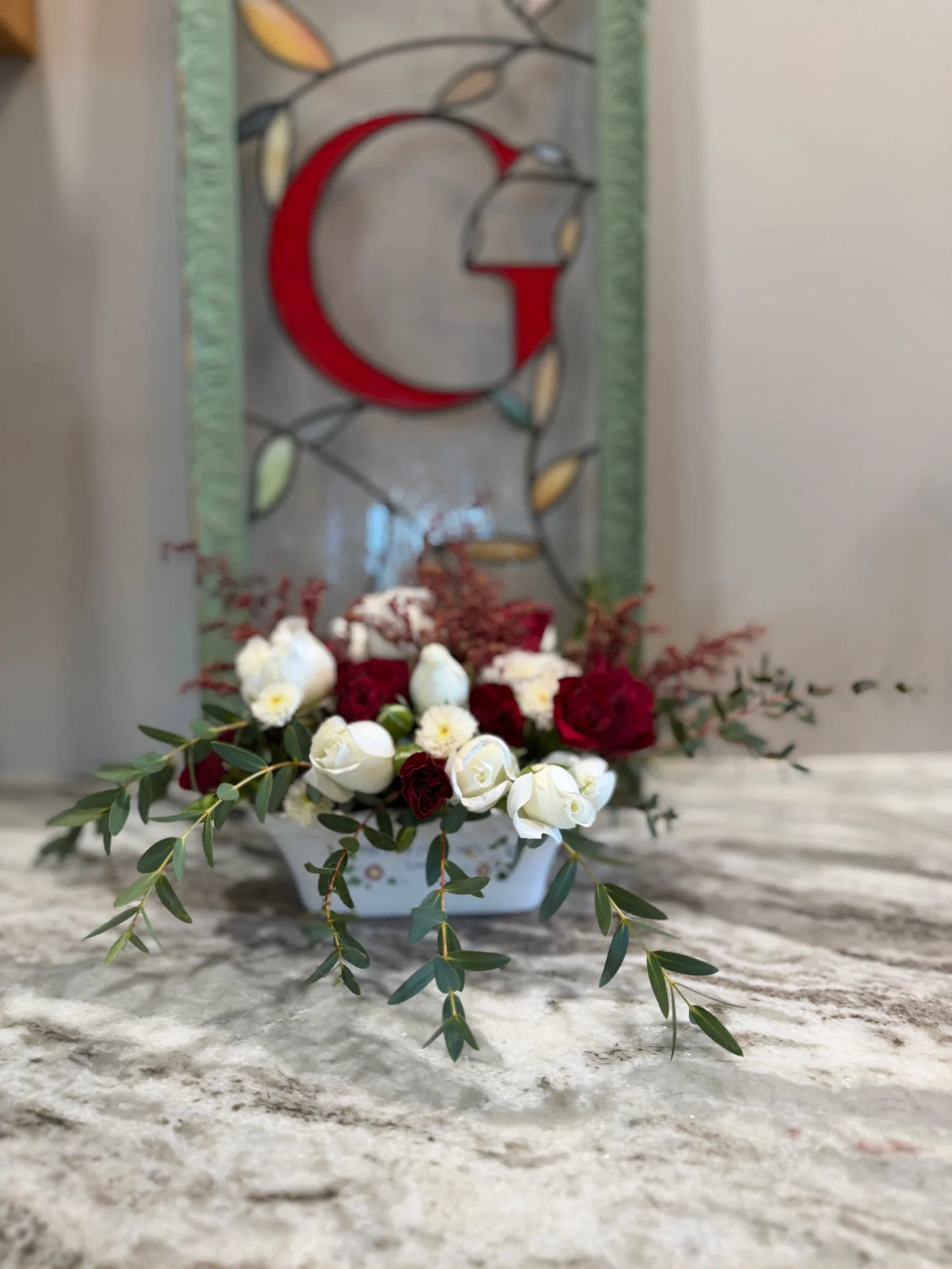 Red and white roses with trailing eucalyptus in a low white dish